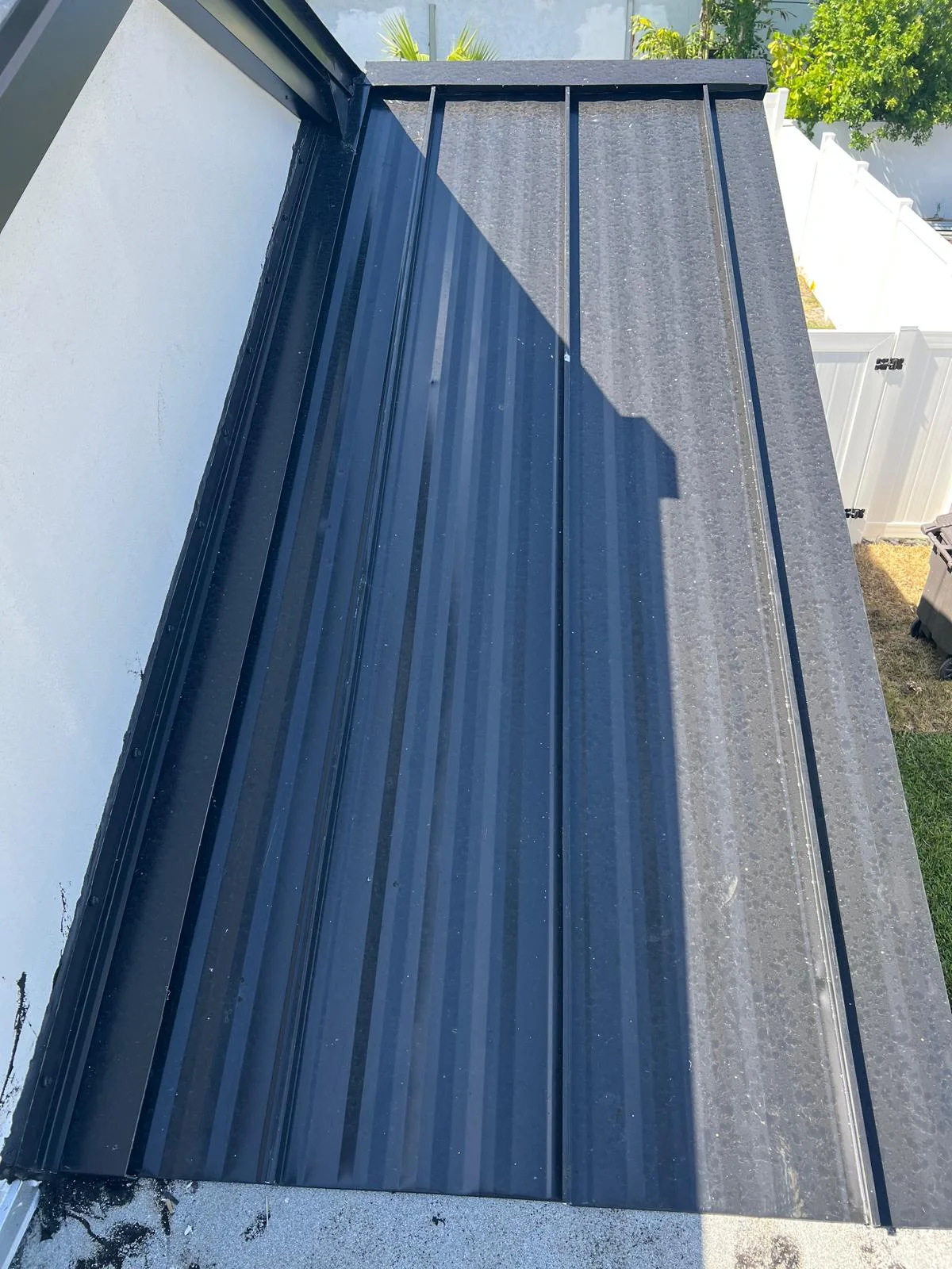 Dark metal corrugated roof panels with angular shadow cast by bright sunlight.