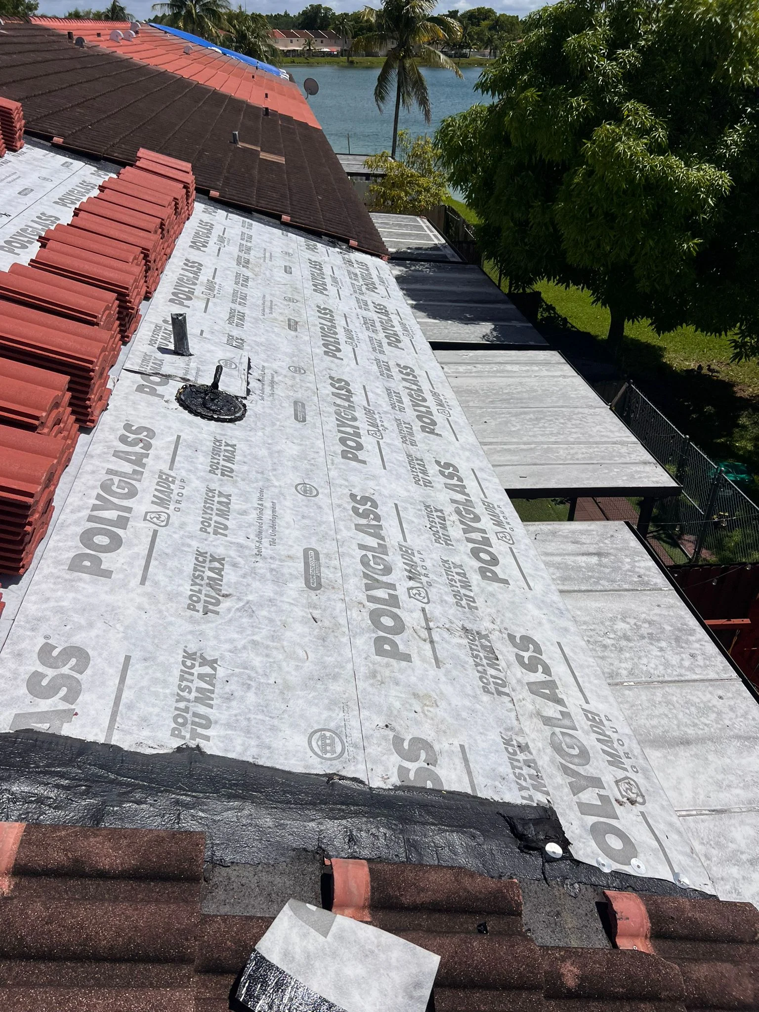 Roof replacement in progress with protective underlayment and red shingles staged nearby.