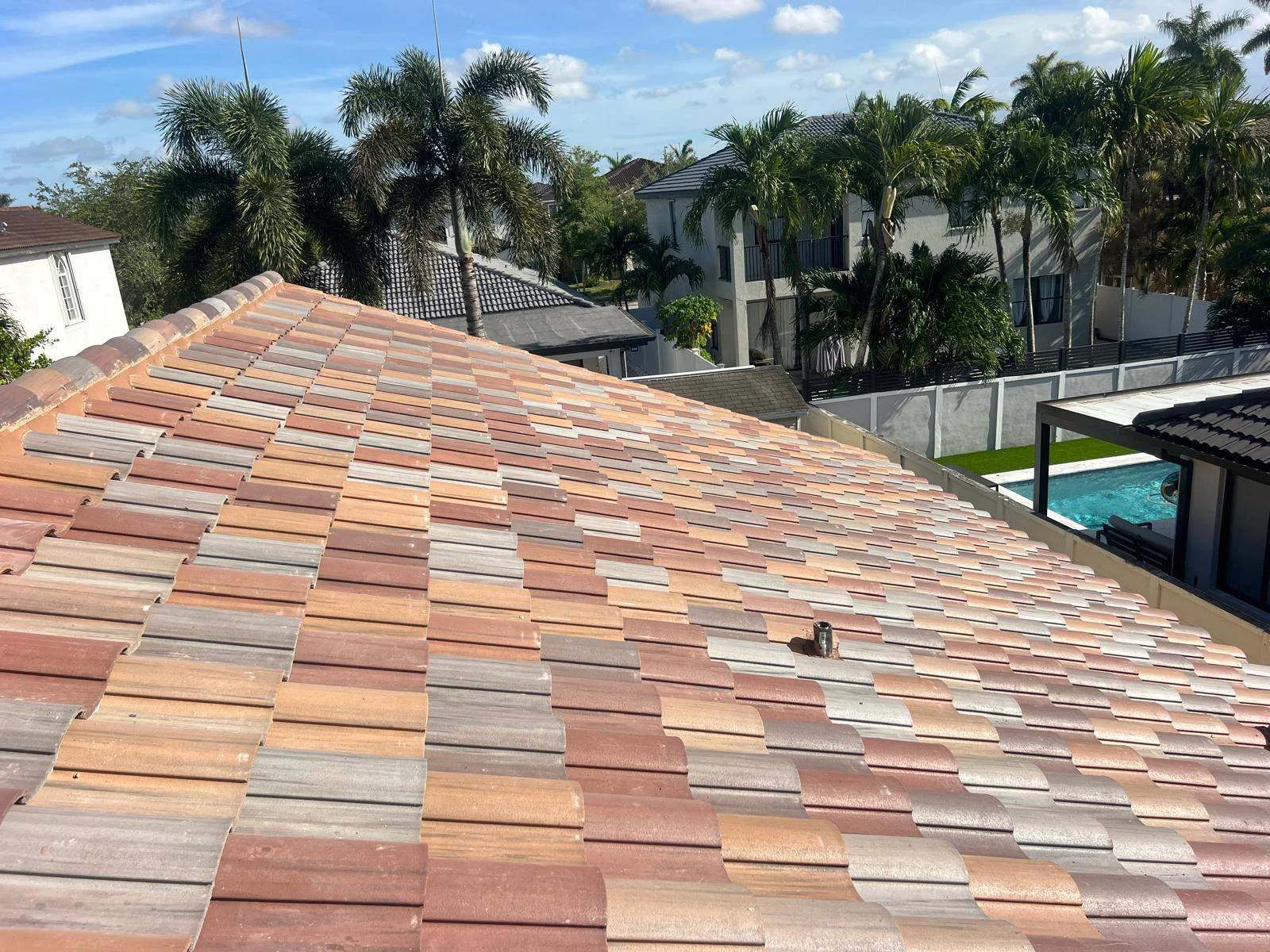 Colorful clay tile roof installation on residential home with tropical palm trees and pool area visible.