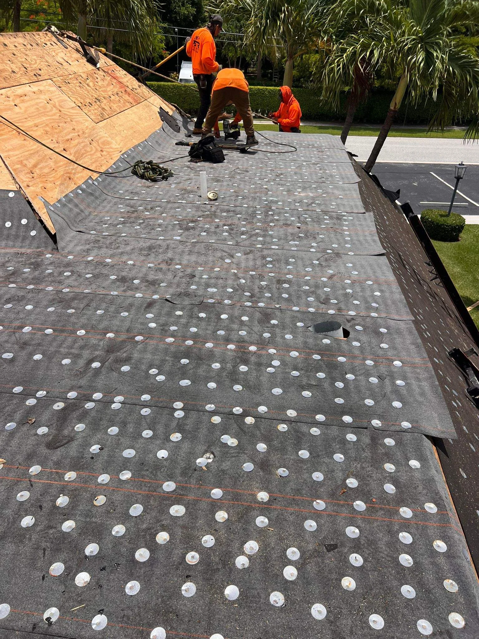 Roofing crew in orange safety gear installs new shingles on residential roof.