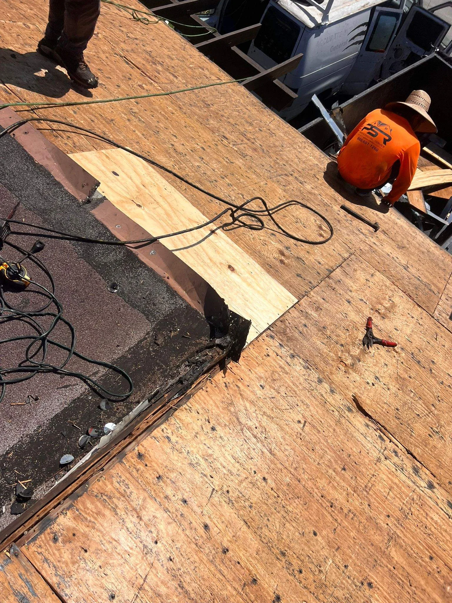 Roofer in orange vest repairs residential roof with plywood patch and shingles.