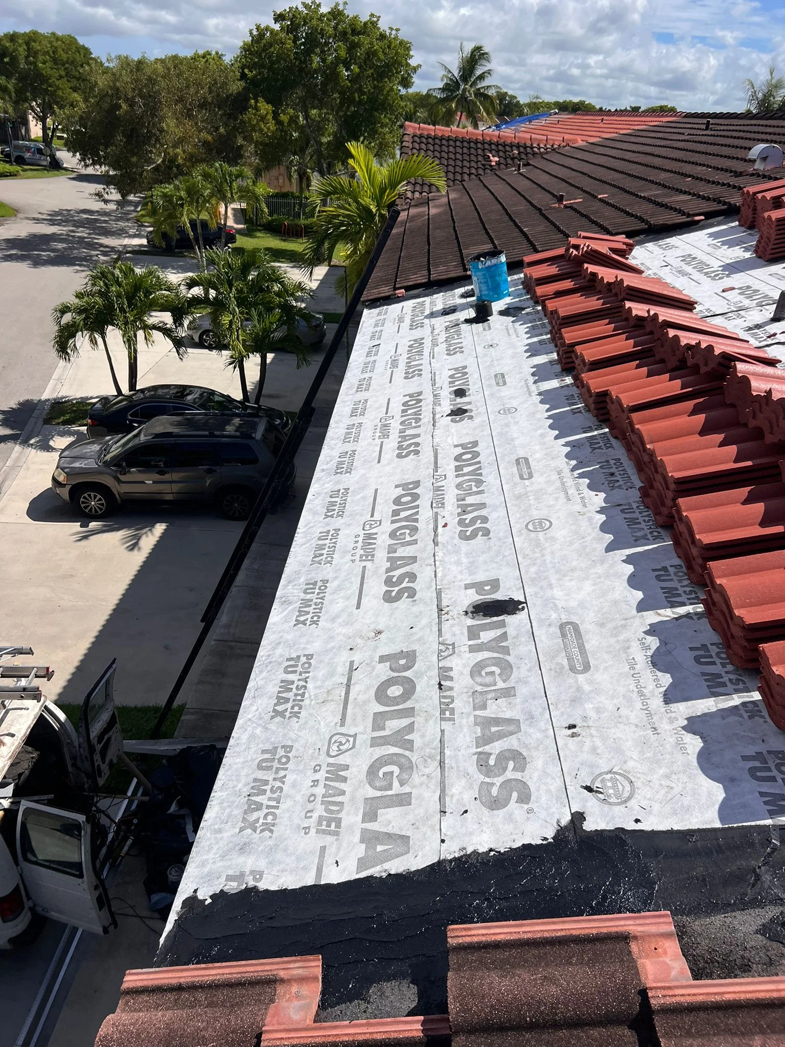 Residential roof installation in progress with underlayment and terra cotta tiles staged.